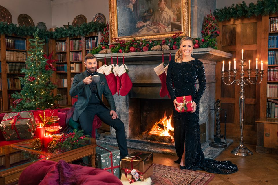 Senkvelds programledere, Stian Blipp og Helene Olafsen klare for Senkvelds Juledugnad. De har pyntet seg og står foran en peis med julegaver.