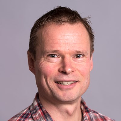 Portrettbilde av Leif Hem, professor ved Norges Handelshøyskole. Han har på seg rødrutete skjorte, og smiler mot kameraet. 