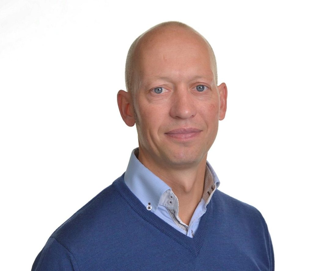 Portrettbilde av Bela Bors, Key Account Manager i Posten Bring. Han har på seg lyseblå skjorte, men mørskeblå genser over. 