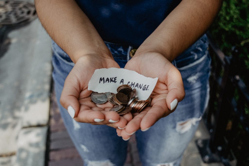 Hender som holder mynter og en lapp der det står "make a change".